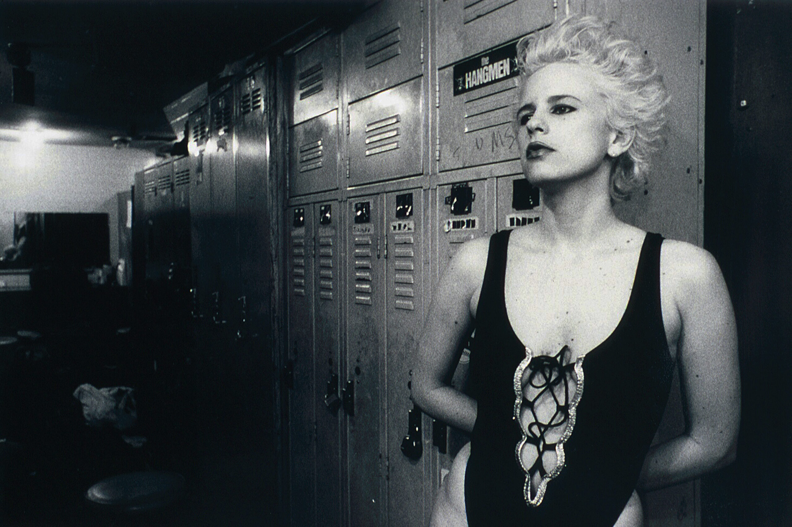 A platinum blonde woman stands in front of lockers, black and white image